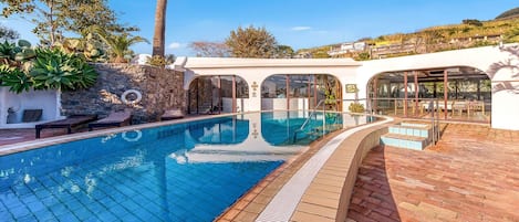 A swimming pool with a tiled deck, surrounded by stone walls and palm trees.