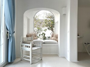 Une pièce avec une fenêtre en arc de cercle peinte en blanc, une chaise blanche et une vue sur la verdure à l’extérieur.