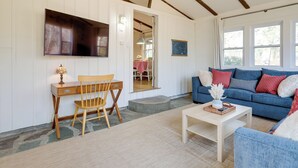 A cozy living room with a wooden desk, a blue sofa, and a television mounted on the wall. - Steps to Beaches & Main Street: Hyannis Retreat (Hyannis)
