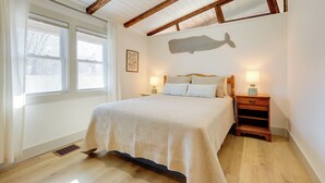 A bedroom with a wooden ceiling, a bed with a white quilt, two bedside tables with lamps, and a wall decoration. - Steps to Beaches & Main Street: Hyannis Retreat (Hyannis)