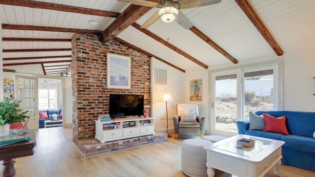 A spacious living room with a brick fireplace, wooden beams, a television, and a blue sofa. - Steps to Beaches & Main Street: Hyannis Retreat (Hyannis)
