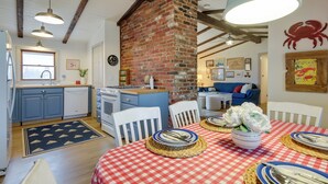 A cozy kitchen with a brick wall, wooden beams, and a dining area set for a meal. - Steps to Beaches & Main Street: Hyannis Retreat (Hyannis)