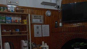 Un coin repas avec une table dressée pour deux personnes, une machine à café, un panier de pain et un panneau indiquant le mot de passe du réseau Wi-Fi.