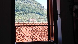 Une fenêtre donnant sur une colline et un bâtiment dont le toit est recouvert de tuiles rouges.