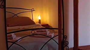 Une pièce avec un lit, une table de chevet et un miroir. Des plantes en pot sont posées sur le sol.