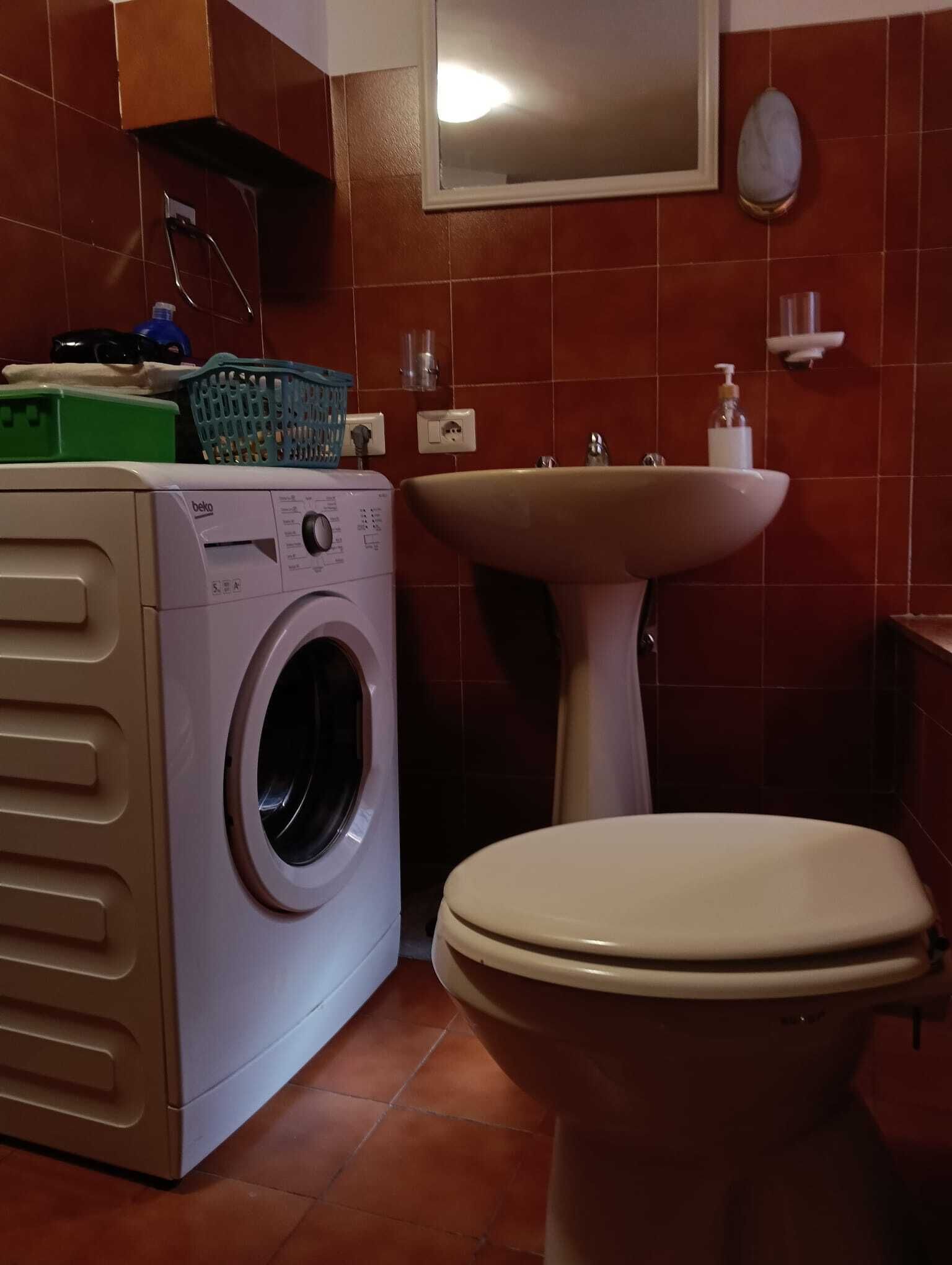 A compact bathroom with a washing machine, a sink, and a toilet.