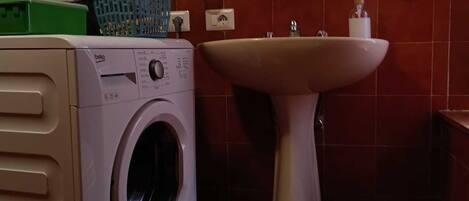 A compact bathroom with a washing machine, a sink, and a toilet.