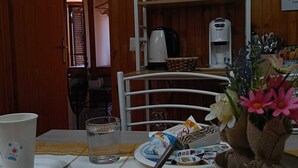 Un coin repas avec une table dressée pour deux personnes, une machine à café et une étagère contenant divers produits alimentaires.