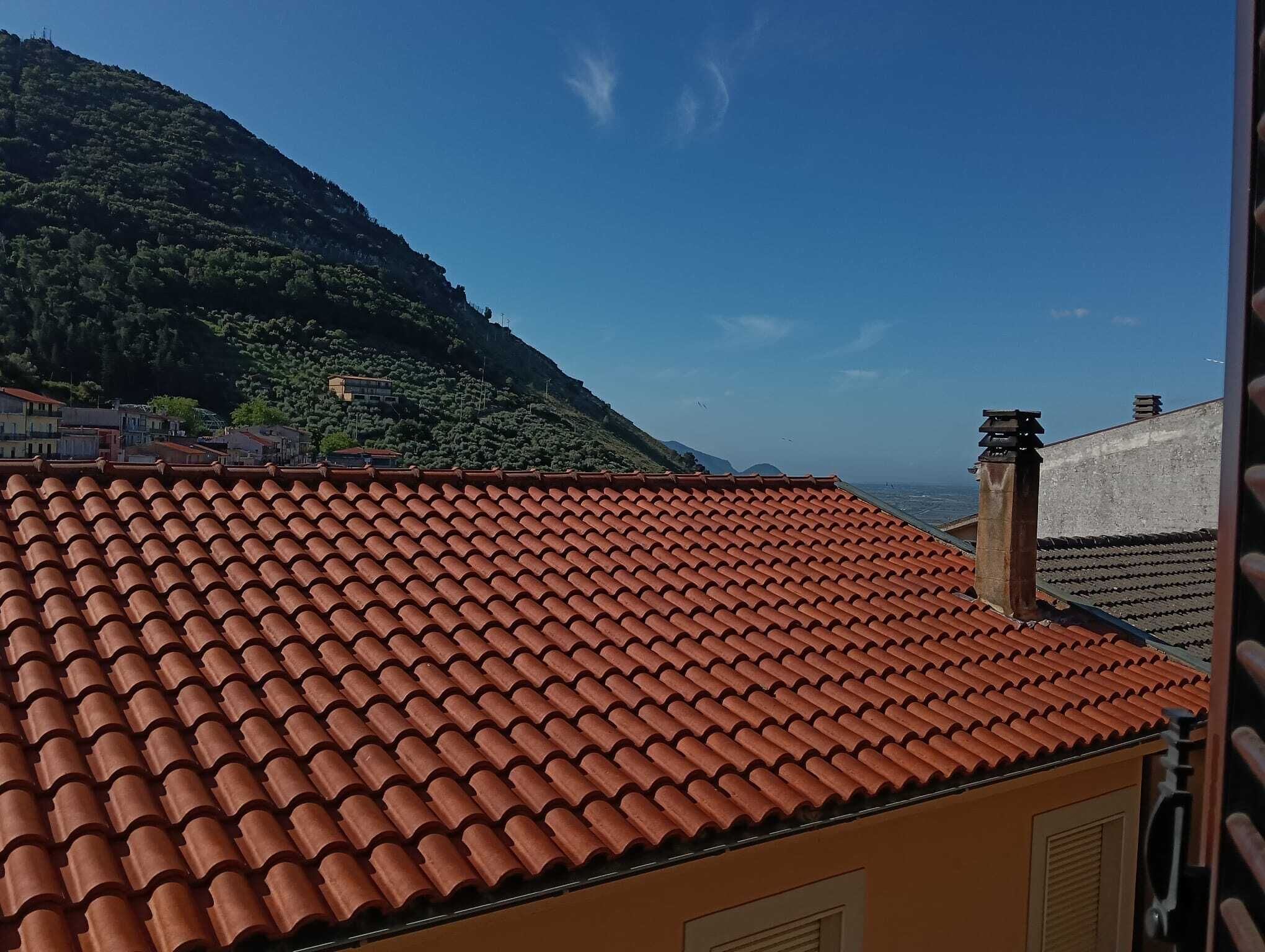 Un bâtiment avec un toit recouvert de tuiles rouges, une montagne en arrière-plan et un ciel dégagé.