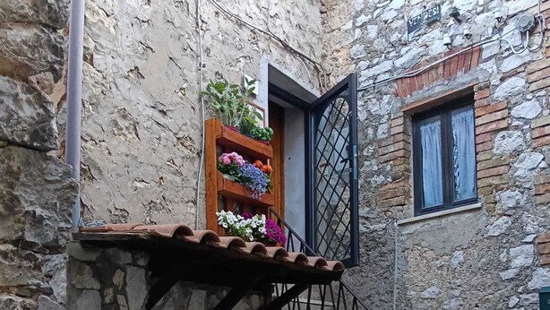 Un bâtiment en pierre avec un escalier en bois menant à une fenêtre protégée par une grille métallique.