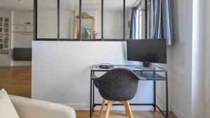 Un salon moderne avec un téléviseur à écran noir posé sur un bureau en verre, un fauteuil noir et un grand miroir qui reflète la pièce.