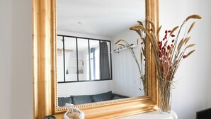 Une pièce avec un grand miroir, une commode blanche, une bougie verte et un vase contenant des plantes séchées.