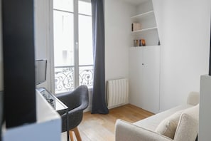 A modern room with a desk, chair, and a sofa. There is a window with a view of the outside, a radiator, and a bookshelf with books. - Modern Apartment - 2br-4p- Canal Saint-martin (Paris)