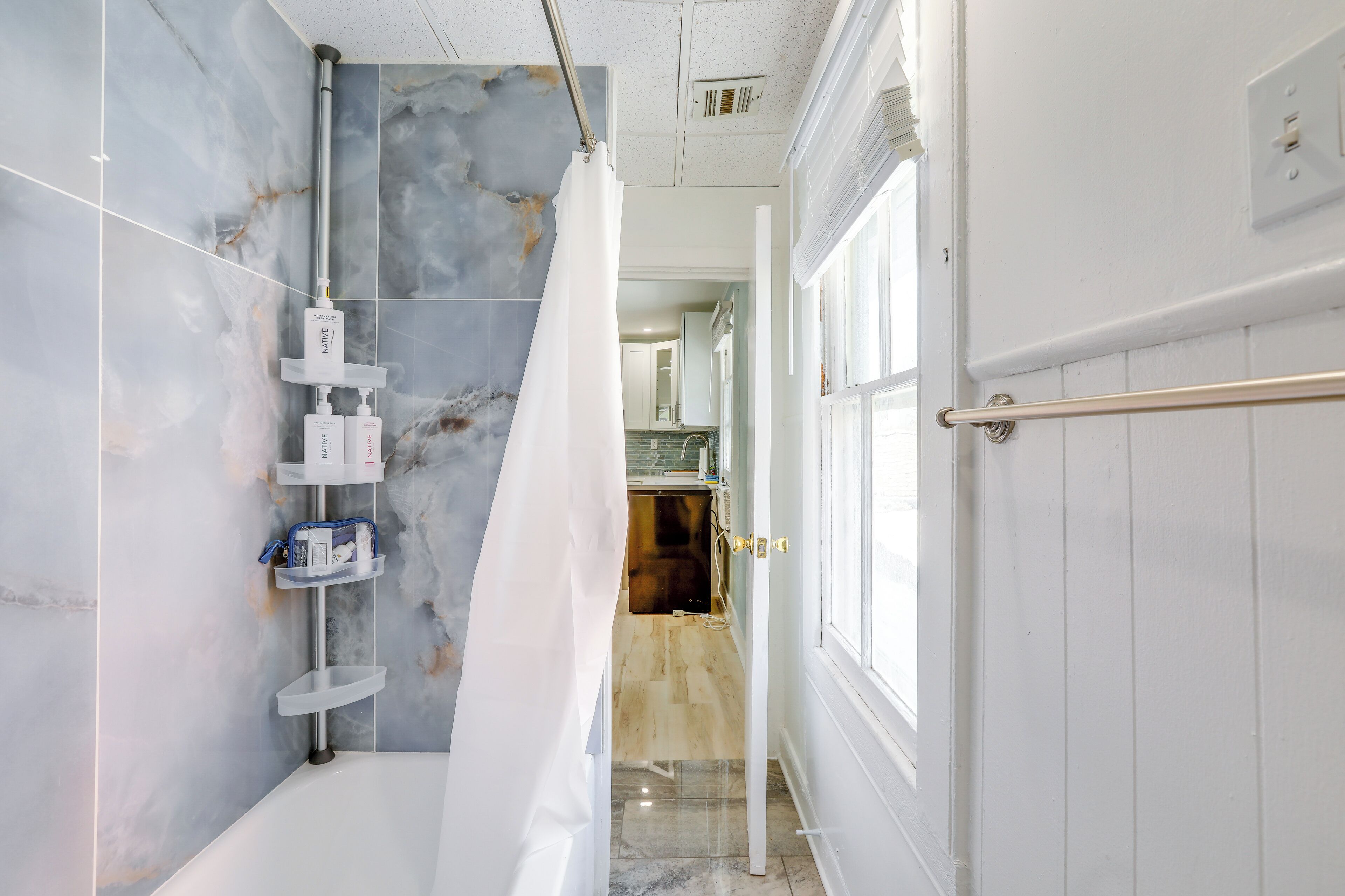 Un baño moderno con ducha, paredes de mármol y vistas a la cocina.