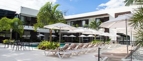 A poolside area with lounge chairs and umbrellas, surrounded by modern buildings and greenery.