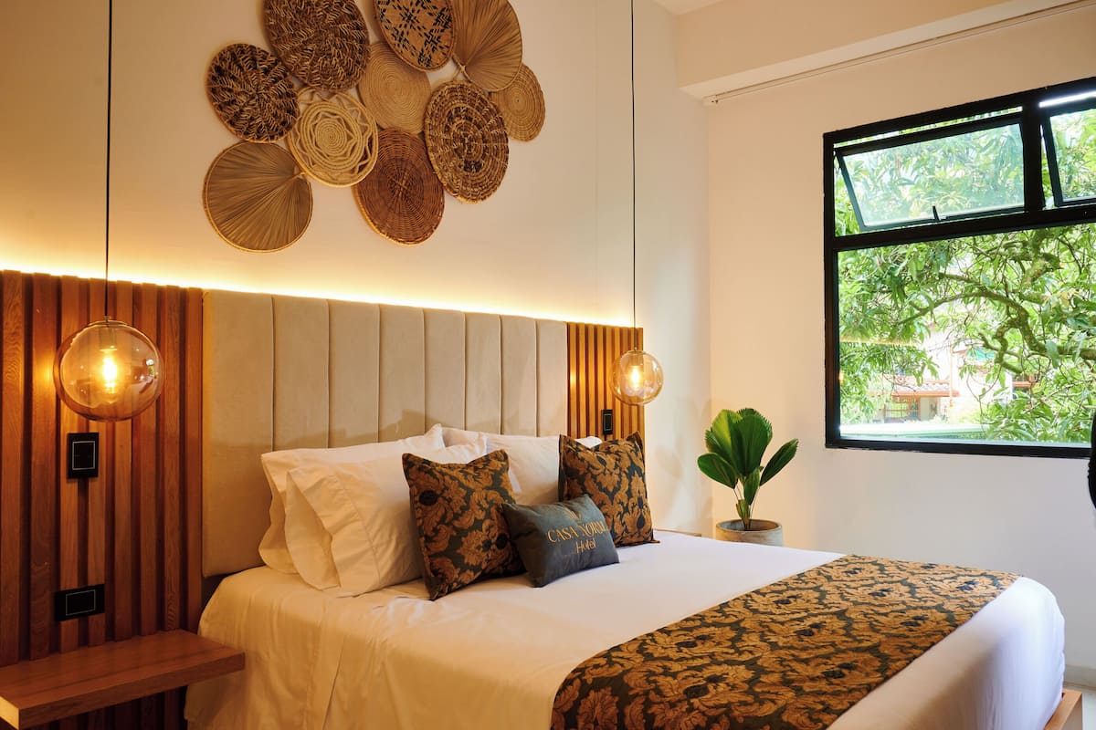 A modern hotel room with a large bed, decorative wall panels, and a window with a view of greenery.