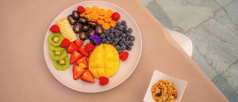 Un plato de frutas variadas y un cuenco pequeño de granola sobre una mesa con textura.