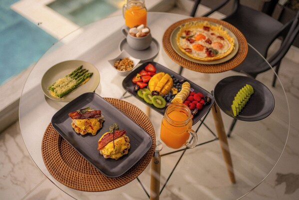 Desayuno con diversos platos y bebidas sobre una mesa junto a una piscina.