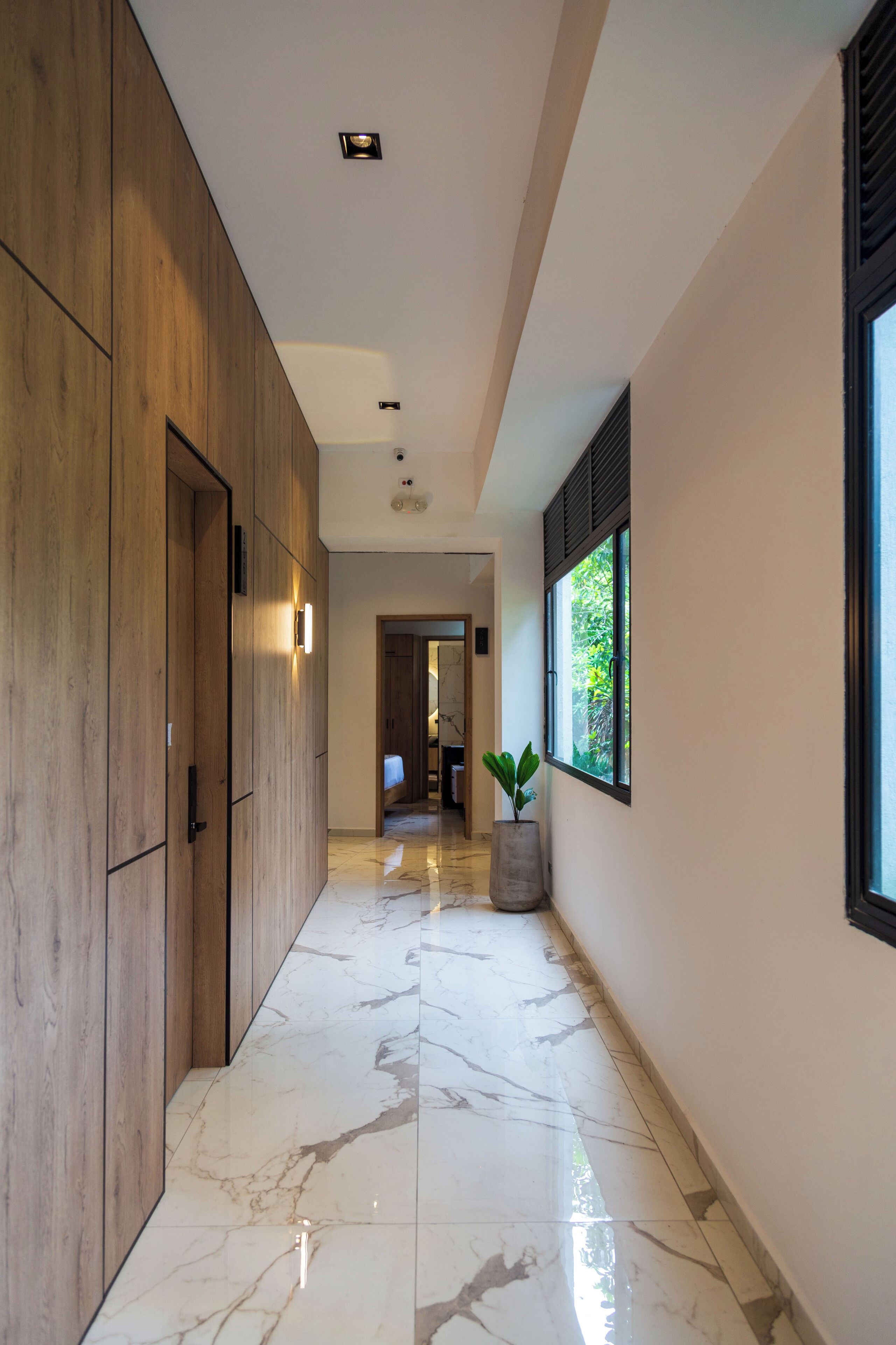 A hallway with wooden paneling, a marble floor, a potted plant, and a window with a view of greenery.