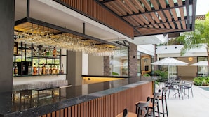 A modern bar area with a wooden counter, bar stools, and a glass display of bottles. - Casa Noral Hotel (Copacabana)