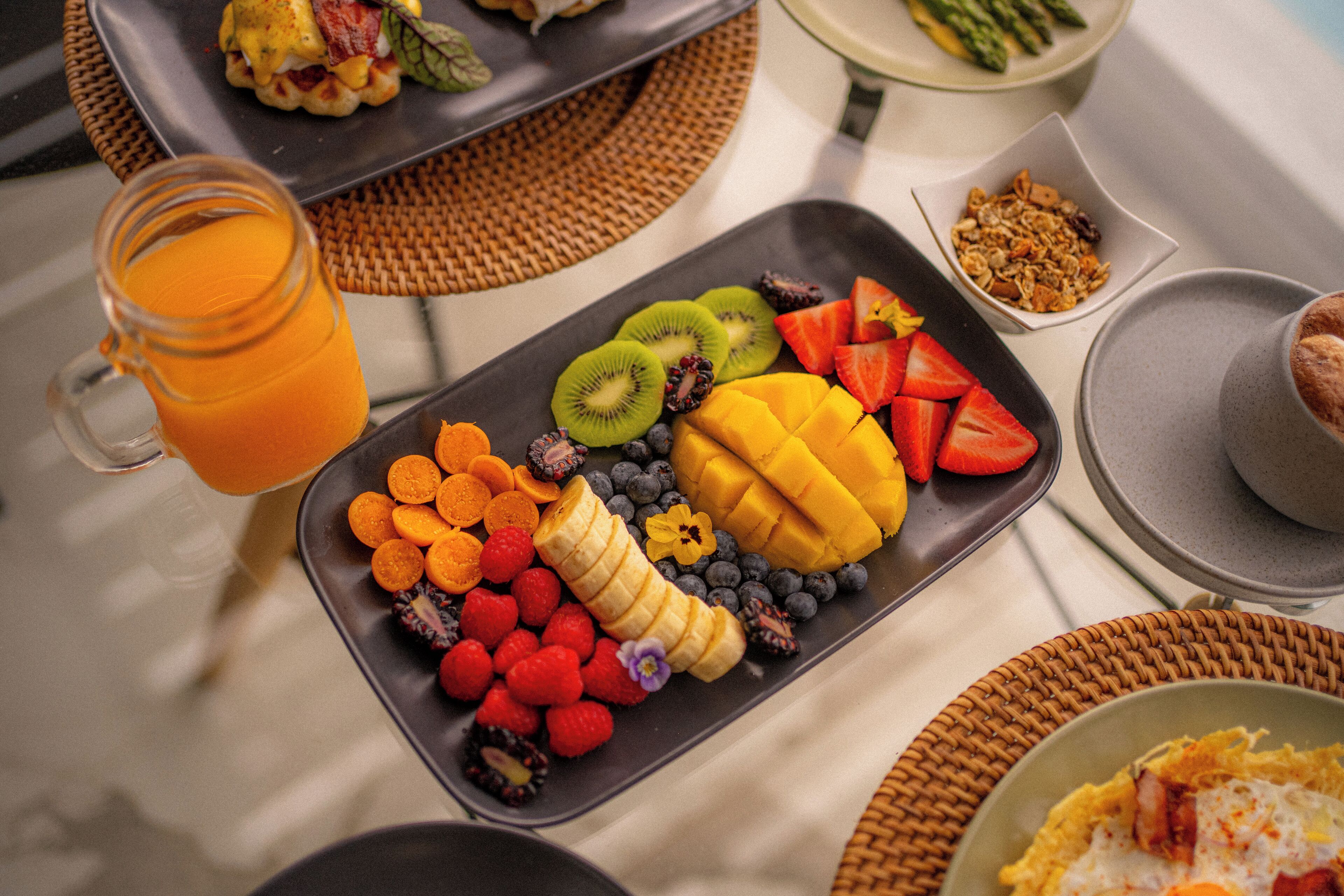 Un bufé de desayuno con una variedad de frutas y un vaso de zumo de naranja.