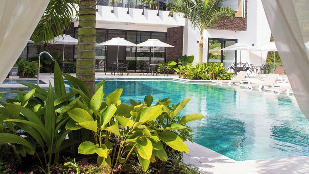 A modern pool area with a clear blue pool, surrounded by lush greenery and white umbrellas. - Casa Noral Hotel (Copacabana)