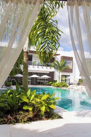 Un área de piscina moderna con una piscina azul cristalina, rodeada de exuberante vegetación y sombrillas blancas.
