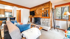 A modern living room with a stone fireplace, wooden accents, and a view of the outdoors. - Hike, Sled & Ski! Cozy Tahoe City Condo w/ Hot Tub (Tahoe City)
