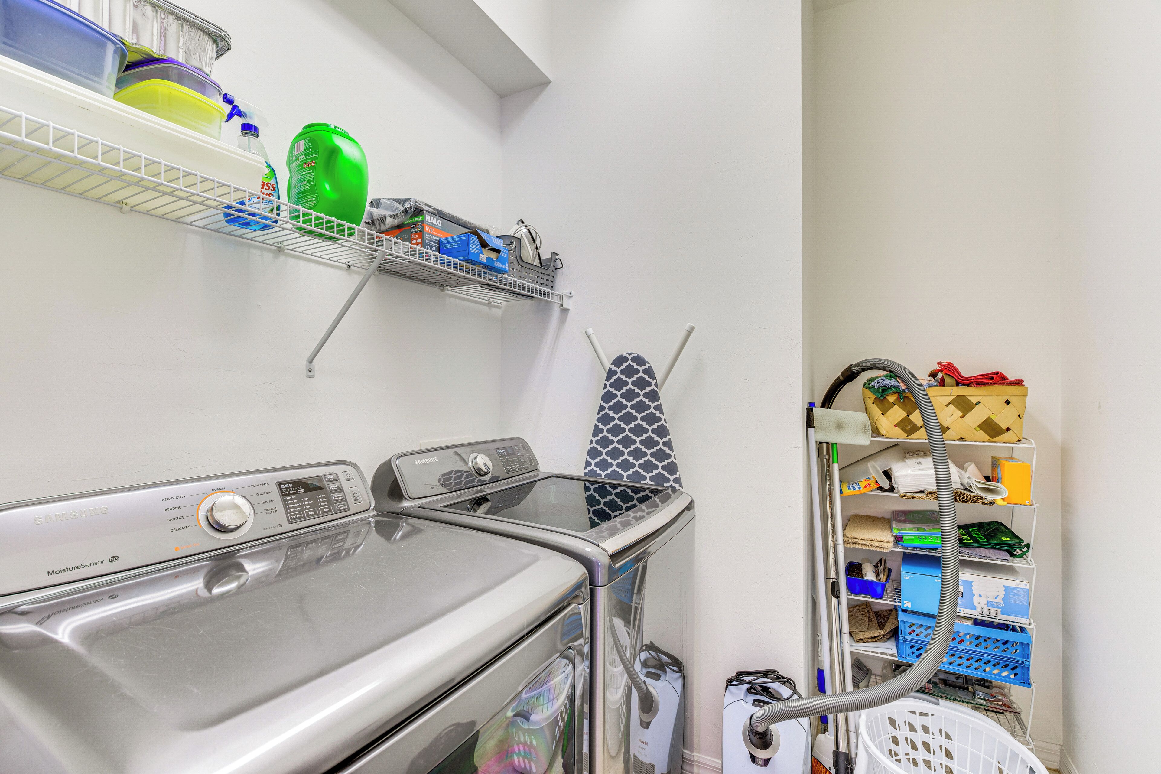 A laundry area with a washing machine, a drying rack, and shelves with cleaning supplies.