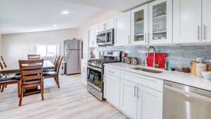 Une cuisine moderne avec des meubles blancs, des appareils en acier inoxydable et un coin repas doté de chaises en bois.