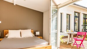 A bedroom with a wooden bed, a small bedside table, and a glass door leading to an outdoor area with a table and chairs. - Ra Sid Spa Loire Sa Vre (Reze)