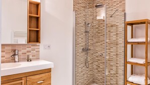 Un bagno moderno con doccia vetrata, un mobile contenitore in legno con specchio e uno scaffale con asciugamani.