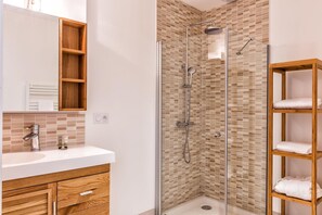 A modern bathroom with a glass-enclosed shower, a wooden vanity with a mirror, and a shelf with towels. - Ra Sid Spa Loire Sa Vre (Reze)