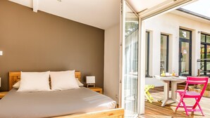 A bedroom with a wooden bed, a small bedside table, and a glass door leading to an outdoor area with a table and chairs.