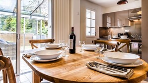 A dining area with a wooden table set for four, a bottle of wine, and a view of the garden through large windows. - Ra Sid Spa Loire Sa Vre (Reze)