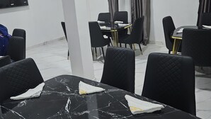 Une salle de conférence avec des tables en marbre, des chaises noires et des rideaux gris.