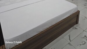 Un lit bien fait, avec une tête de lit en bois, une table de chevet avec une lampe et un climatiseur fixé au mur.