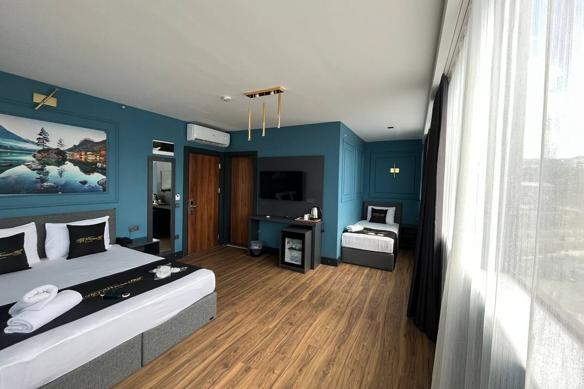 A modern hotel room with a large bed, a TV, a desk, and a painting on the wall.