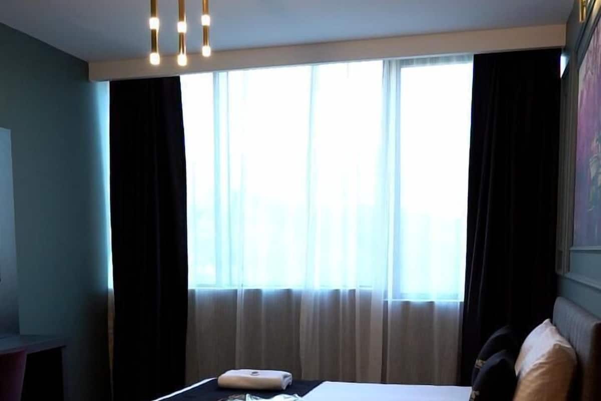 A hotel room with a bed, bedside tables, a desk, a chair, and a window with curtains.