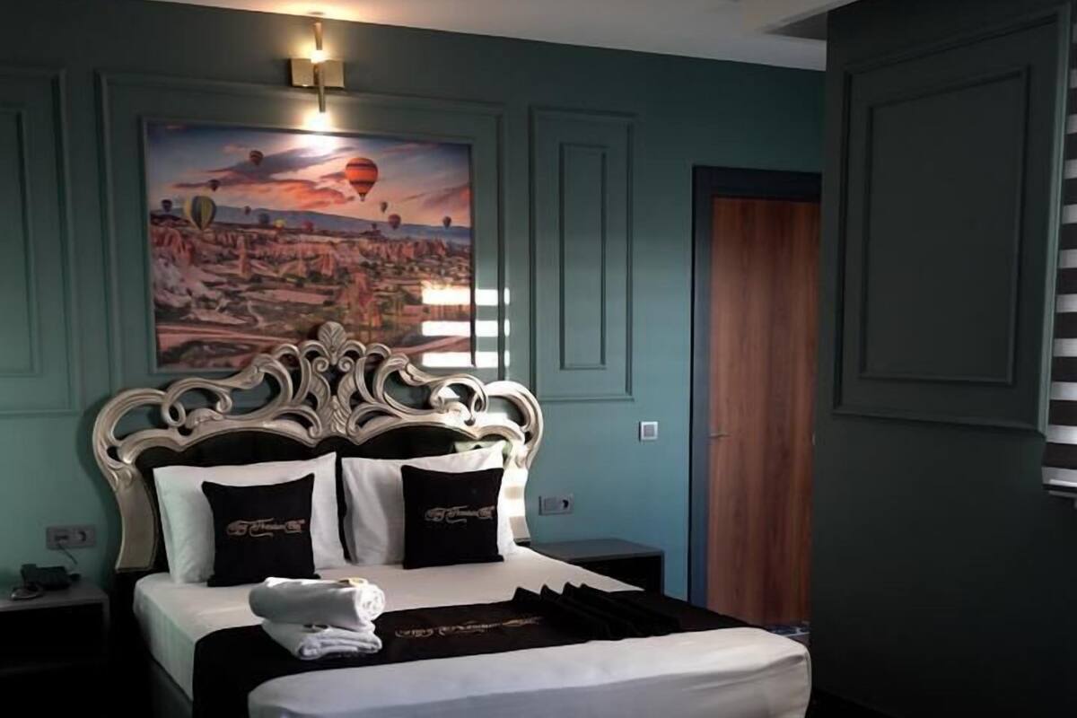 A bedroom with a large bed, a chandelier, a painting on the wall, and a wooden floor.