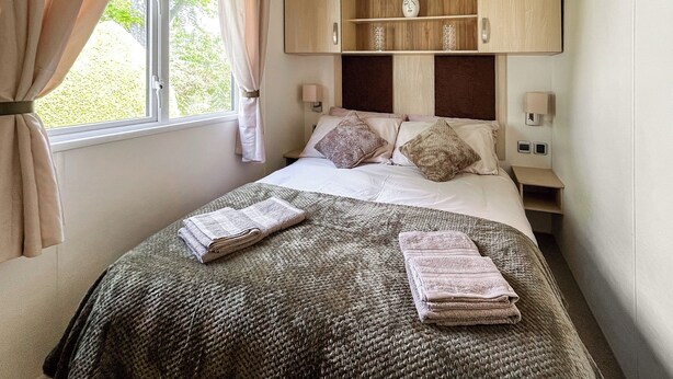 A neatly made bed with a grey knitted blanket, a wooden headboard, and a bedside table with a lamp. - 3 bedroom accommodation in Ruthin and the Clwydian Range (Ruthin and the Clwydian Range)