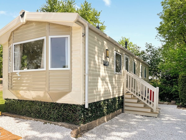 A single-story mobile home with a covered porch, a staircase, and a small garden area.