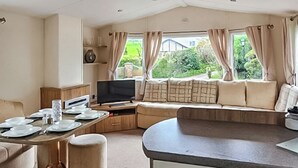 A compact room with a dining table, a sofa, a television, and a window with curtains. - 3 bedroom accommodation in Ruthin and the Clwydian Range (Ruthin and the Clwydian Range)