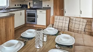A compact kitchen with a stove, oven, and microwave, a dining table set with white plates and a clear glass pitcher, and a sofa with plaid cushions. - 3 bedroom accommodation in Ruthin and the Clwydian Range (Ruthin and the Clwydian Range)