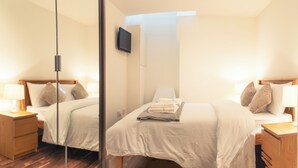 A hotel room with two beds, a flat-screen TV mounted on the wall, and a glass partition. - Entire Family Apartment- Edinburgh (Edinburgh)