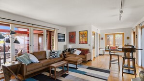 A spacious living area with a brown leather sofa, a wooden coffee table, and a striped rug. There are two black floor lamps and a ceiling fan.