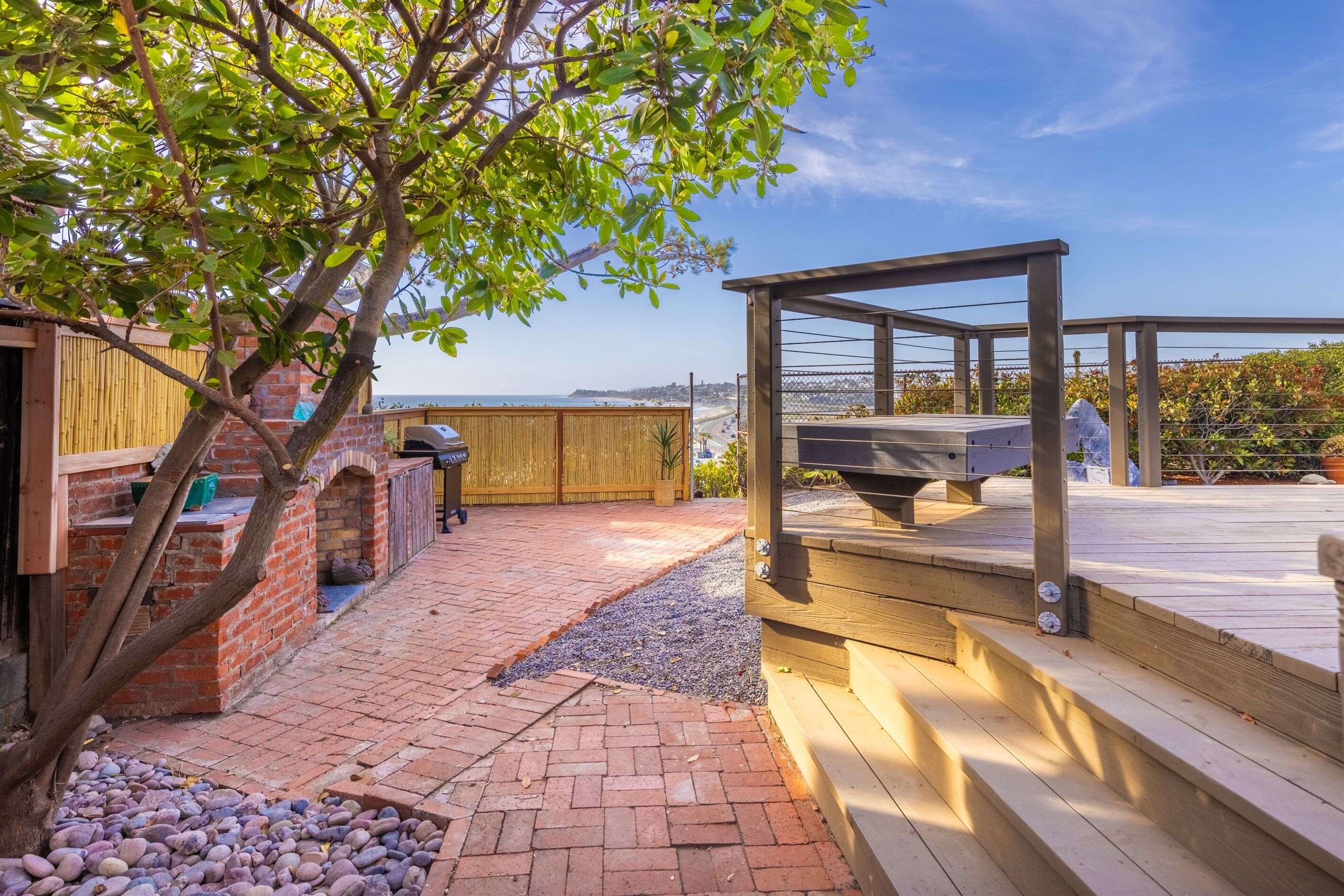 Un área de patio con terraza de madera, una parrilla y vista a la playa.