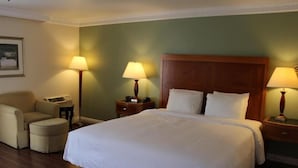 Ett hotellrum med en stor säng, två sängbord med lampor, en stol och ett litet bord med en telefon.