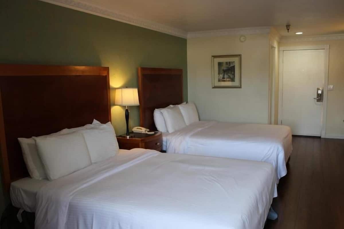 A hotel room with two beds, a nightstand with a lamp, and a door.