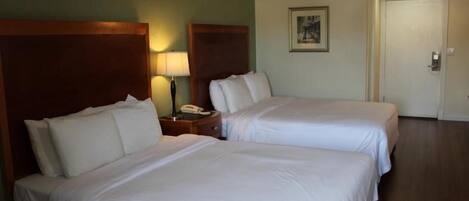 Una habitación de hotel con dos camas, una mesita de noche con lámpara y una puerta.